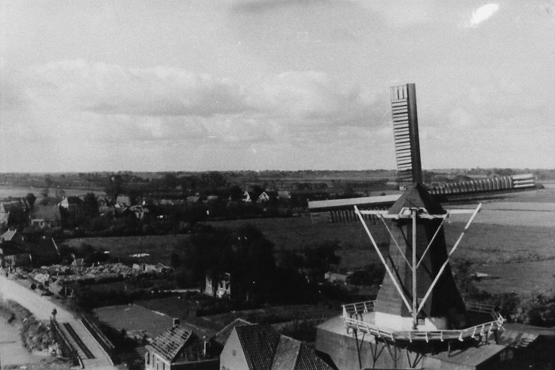 3, Molen 00628 De Hoop (Holwierde), Herkomst: Reproductie, de foto hangt in de kerk van Holwierde.Toelichting: Zicht op de molen vanuit de kerk, kort na de bevrijding. Rondom is er nog oorlogsschade te zien. Boven de noodbrug de resten van de boerderij, die in de film Stoere Werkers was te zien. Foto M.E. van Doornik, opname 24-04-2010 | Database Nederlandse molens media-bestand