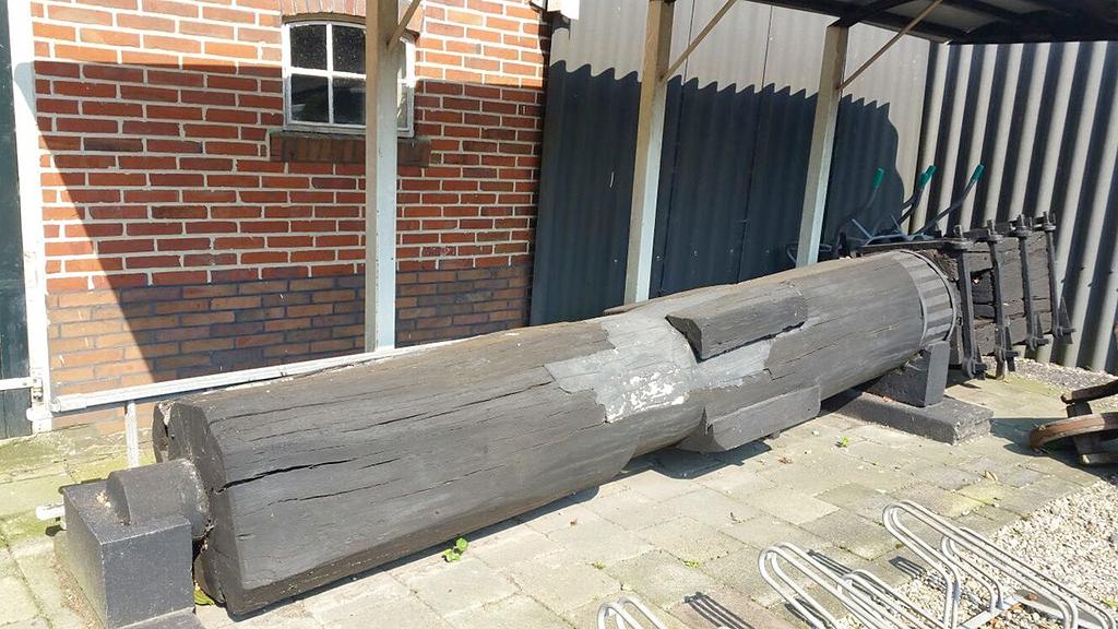 1, As g.n., onbekend, Pieter Zuijkerbuijk (30-8-2016)De houten bovenas van voor de grote restauratie in de jaren ’70 wordt naast de molen bewaard. | Database Nederlandse molens media-bestand